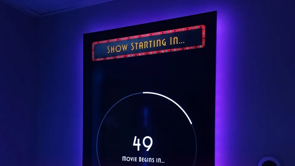 Cartelera digital DMB en un muro con luz violeta: en la pantalla, la cuenta regresiva «Show starting in…» con el número 49 antes de la función.