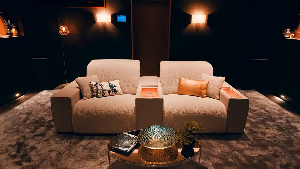 Sofá de cine Moovia en tela beige con consola central iluminada, en una sala oscura con luz cálida.