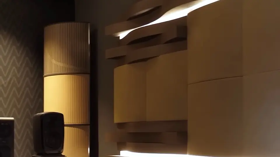 Sala de muestra Univicoustic: columna difusora curva de madera clara y paneles ondulados con luz indirecta, junto a un monitor de estudio.