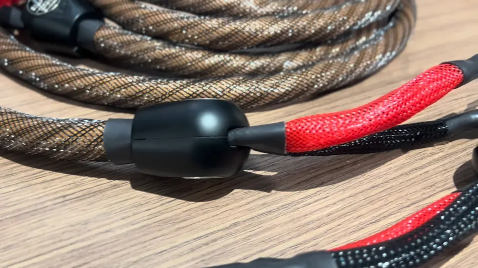 Cable de bocina Wireworld trenzado en café con divisor negro y ramales rojo y negro, sobre una mesa de madera.